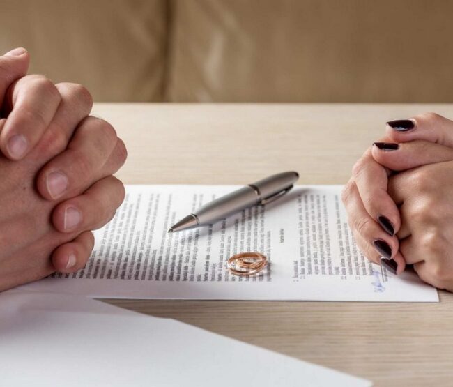 Couple sitting across from each other with divorce papers and rings on the table.