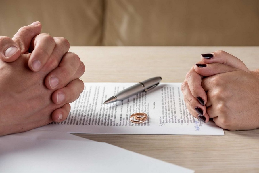 Couple sitting across from each other with divorce papers and rings on the table.
