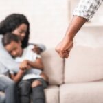 Mother protecting child on couch while facing an aggressive partner during a domestic violence incident.
