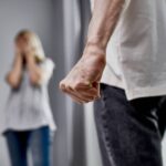 Man with clenched fist in foreground and distressed woman in background representing domestic violence and custody issues.