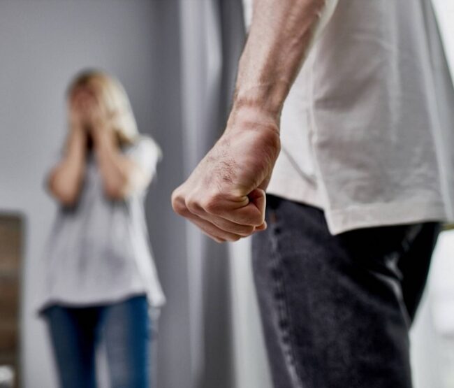 Man with clenched fist in foreground and distressed woman in background representing domestic violence and custody issues.